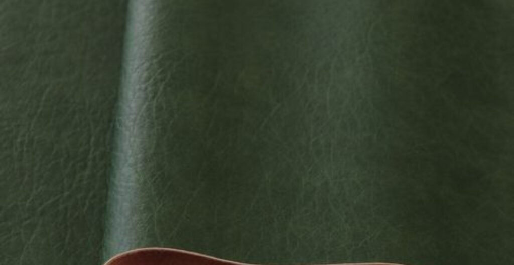 Close-up of plant-based leather in a deep green color with a contrasting light brown edge.
