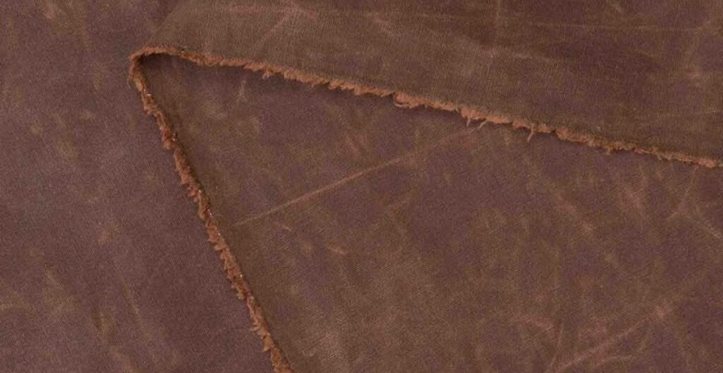 Close-up of waxed canvas fabric in a rich brown color, showing frayed edges.