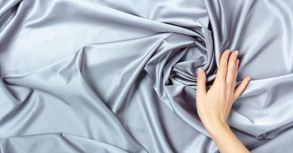 Luxurious silver charmeuse fabric with a silky, smooth texture and a soft draped effect.