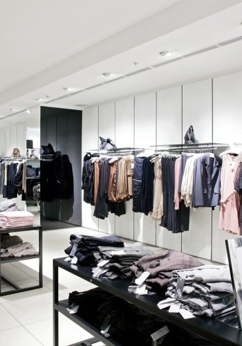 A modern clothing store interior featuring clothing displays on racks and folded items on tables.