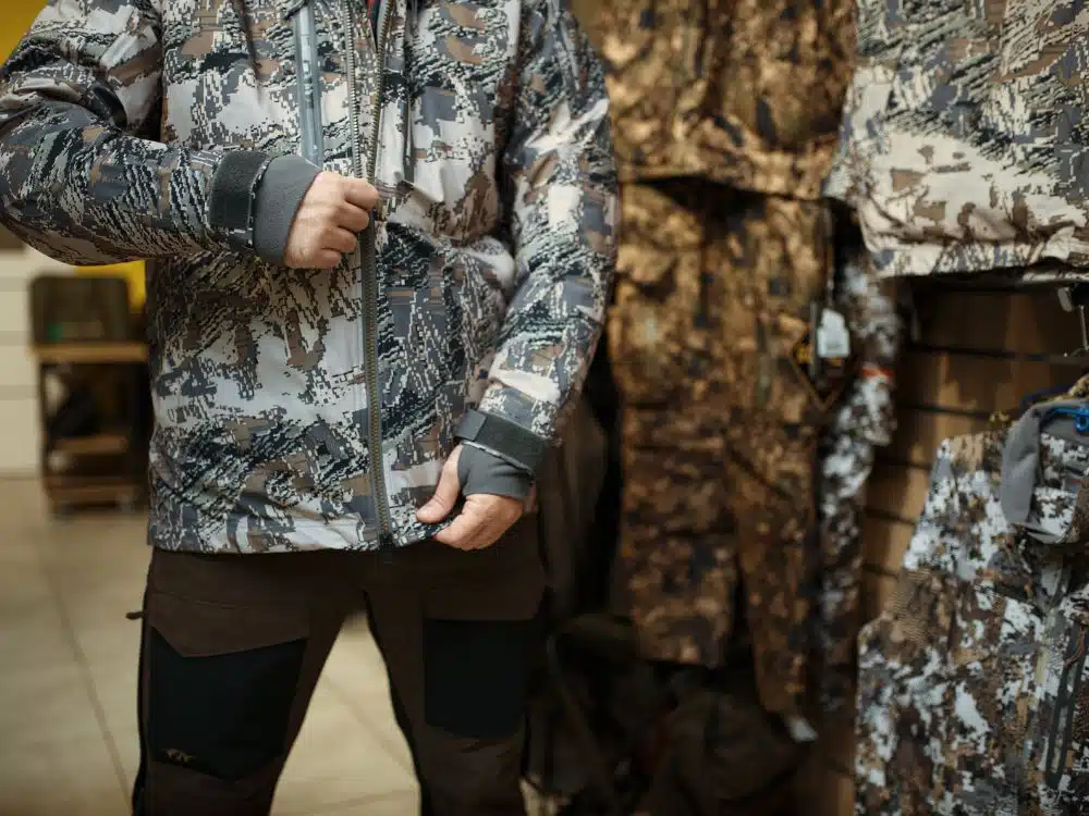 Close-up of a person wearing a camouflage jacket in a clothing store with hunting gear.