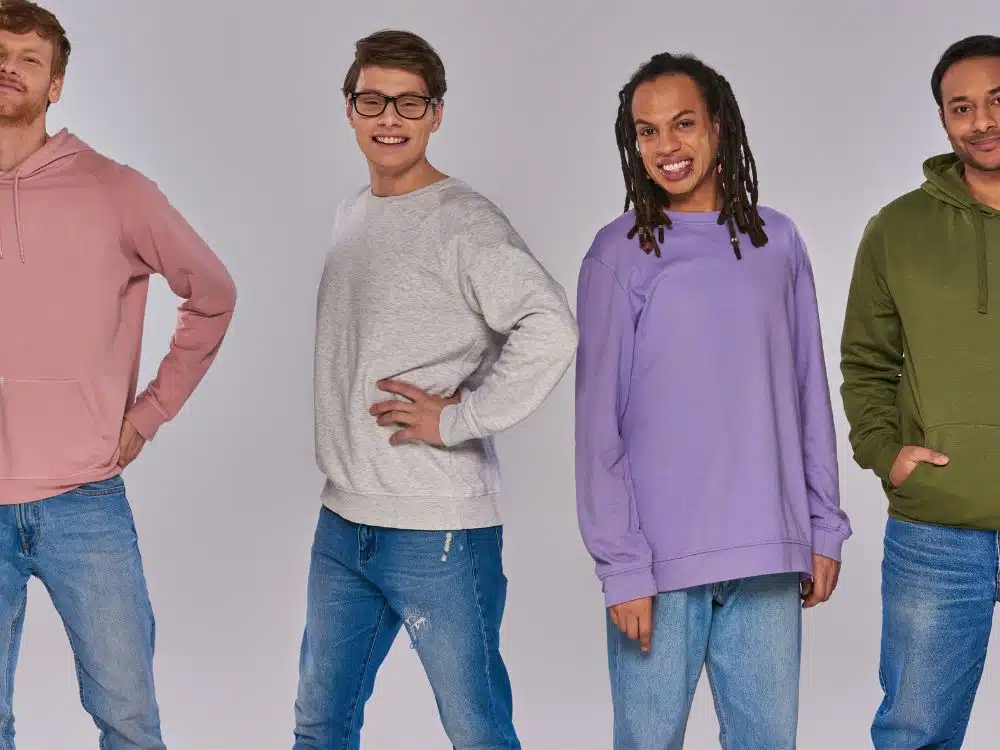 Four young men wearing colorful sweatshirts and jeans, posing against a neutral background.