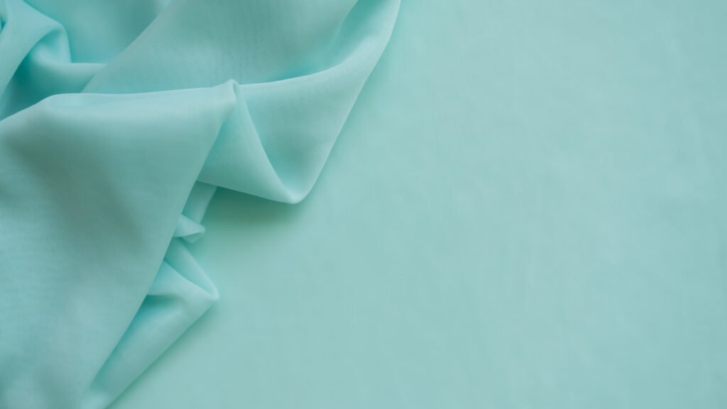 A piece of light blue chiffon fabric is gently draped over a smooth, matching background.