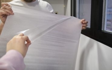 A person is gently holding a piece of chiffon fabric, showcasing its delicate and translucent nature during a pressing process.