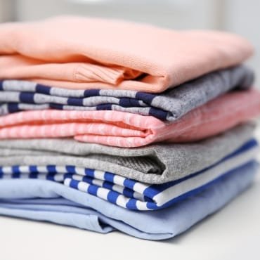 A neatly folded stack of cotton clothing in various colors, including pink, gray, and blue.