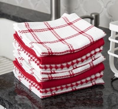 A stack of cotton dish towels in red and white patterns on a dark countertop.