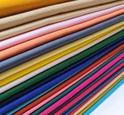 This image showcases a vibrant array of folded fabric swatches in various colors, highlighting their texture and quality. The fabrics appear to be ideal for making cotton curtains and upholstery.
