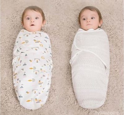 Two swaddled babies, one in a patterned blanket and the other in a plain white blanket, both looking surprised.