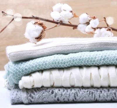 A neatly stacked arrangement of folded cotton garments in various shades, with a cotton branch adorned with fluffy cotton bolls in the background.