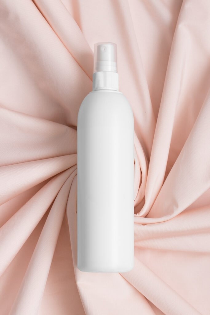 A white spray bottle placed on a soft, pink fabric background.