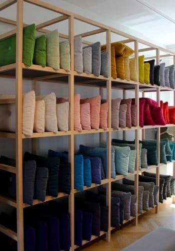 A wooden shelf displaying an assortment of cotton cushions in multiple colors, arranged in neat rows.