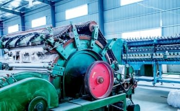 A large cotton ginning machine in an indoor facility, featuring various mechanical components and a prominent red wheel.