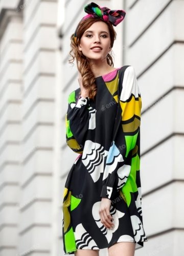 Model in a colorful graphic print tee dress with long sleeves and a matching headband, posing in front of a modern building. 