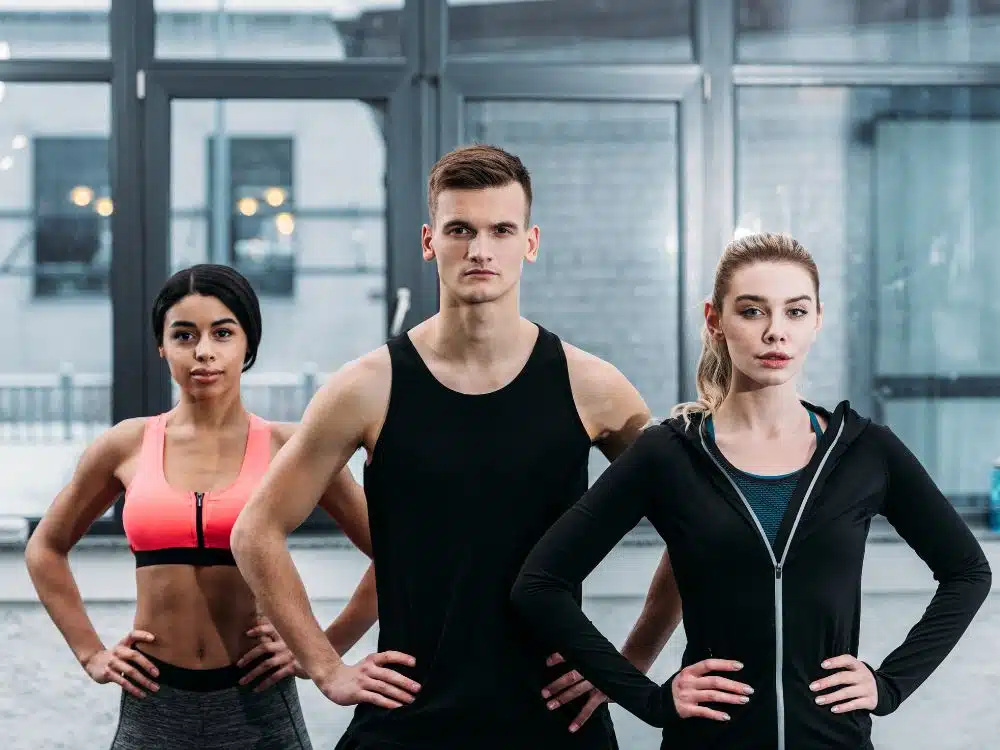 Three athletic individuals posing confidently in a gym environment.