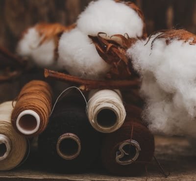 Spools of thread in various colors alongside cotton bolls.