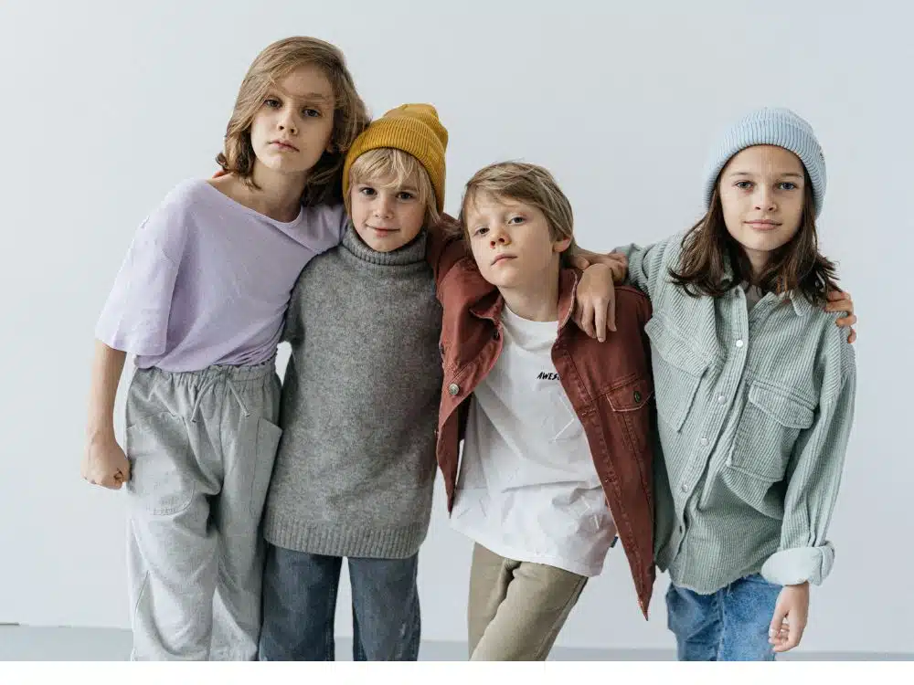 Four children posing together in casual winter fashion in a studio setting.