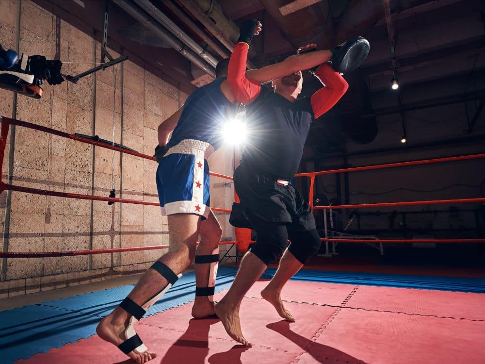 Two fighters practicing techniques in a boxing ring with dramatic lighting.