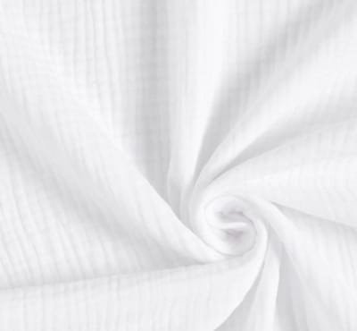 Close-up of white muslin fabric, showcasing its soft texture and fine pleats.