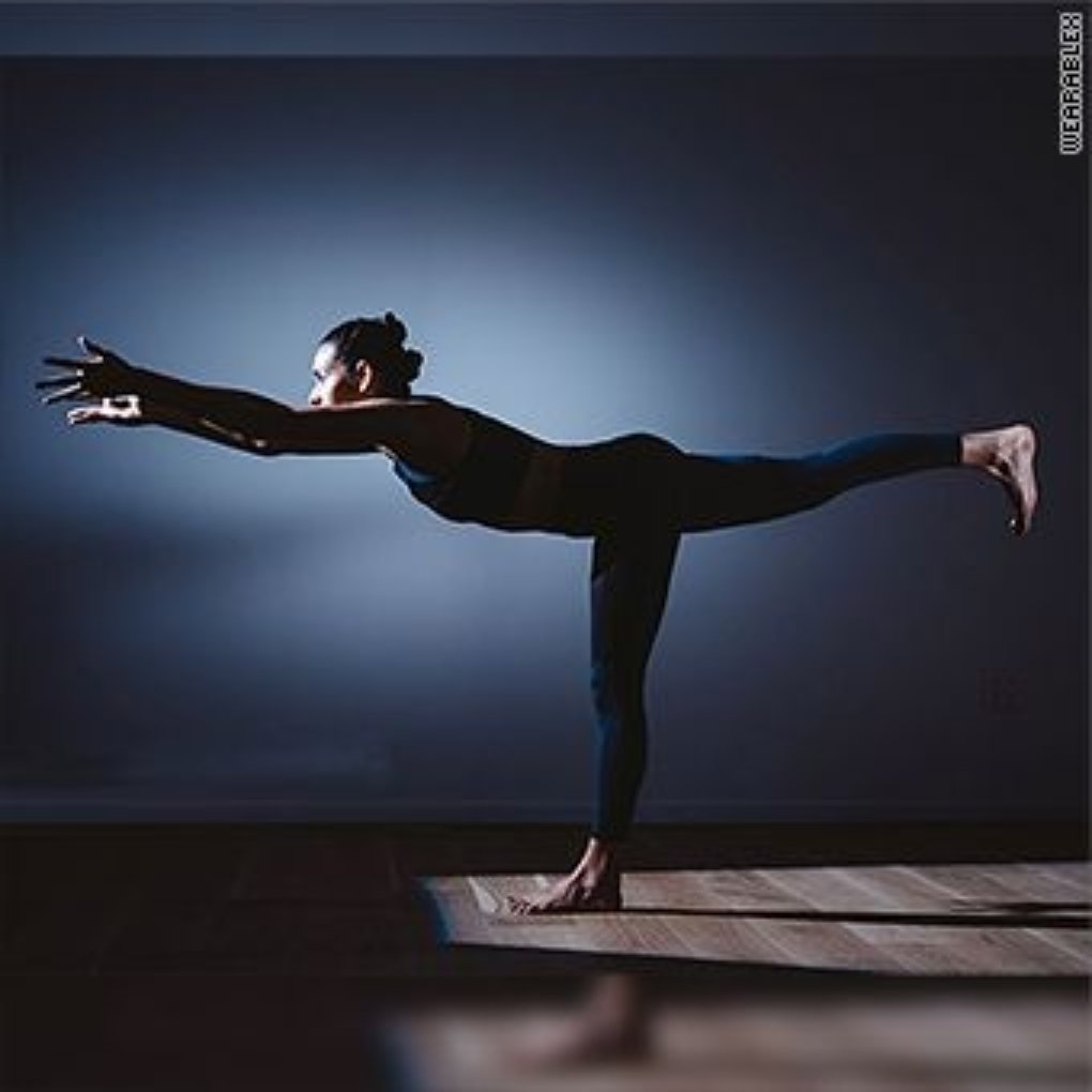 A woman practicing yoga in a dynamic pose, extending her arms and one leg in a dimly lit room.
smart sports wear
