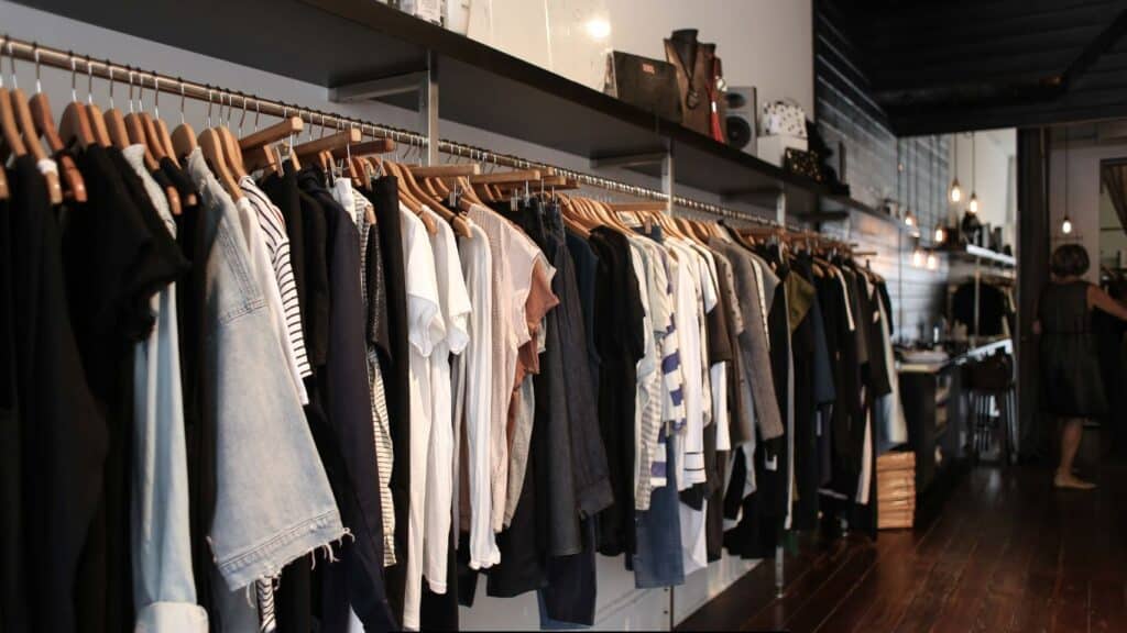A stylish sample room space featuring a variety of clothing items neatly hung on wooden hangers. The collection includes casual wear like t-shirts and denim, showcasing our products in a modern and inviting environment. Soft lighting and minimalistic decor enhance the shopping experience.