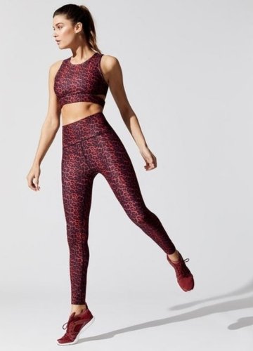 A woman wearing a red leopard-print sports bra and matching leggings, mid-stride in a dynamic pose, paired with red athletic shoes.