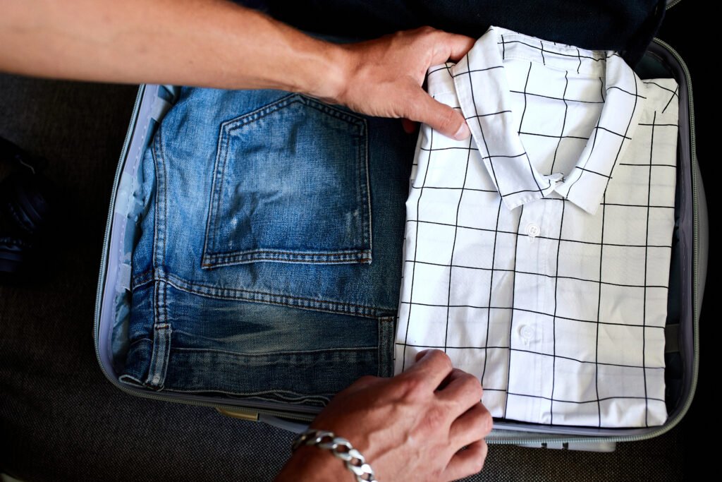 A person packing a suitcase with a white checkered shirt and a pair of blue jeans. Wrinkle-Free Shirts