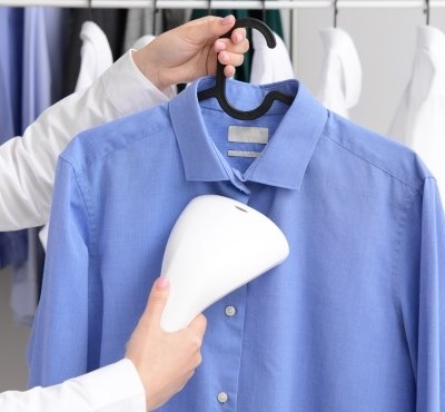 Person using a handheld steamer on a blue shirt hanging on a hanger.