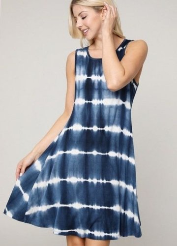 A woman wearing a sleeveless tie-dye dress in shades of navy and white, smiling as she holds the hem of the dress.