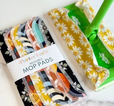 A pack of reusable cotton mop pads with colorful, patterned fabrics next to a green mop handle with a floral cotton cover and a green mop bucket. Indirect Uses of Cotton 