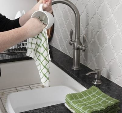 A person drying a cup with a dish towel near a sink.