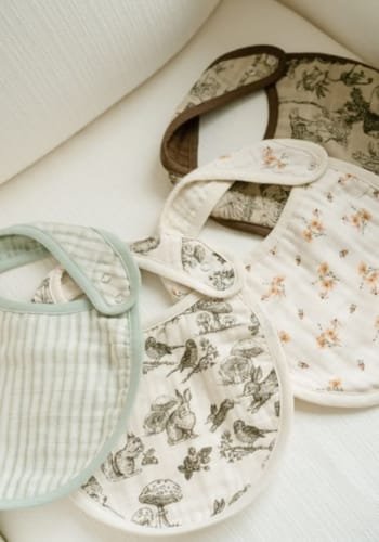 A selection of baby bibs in various designs, including floral patterns and animal prints, displayed on a soft surface.