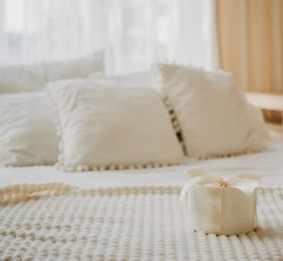 A neatly made bed with plush white pillows and a small gift box wrapped in a ribbon on a textured blanket.