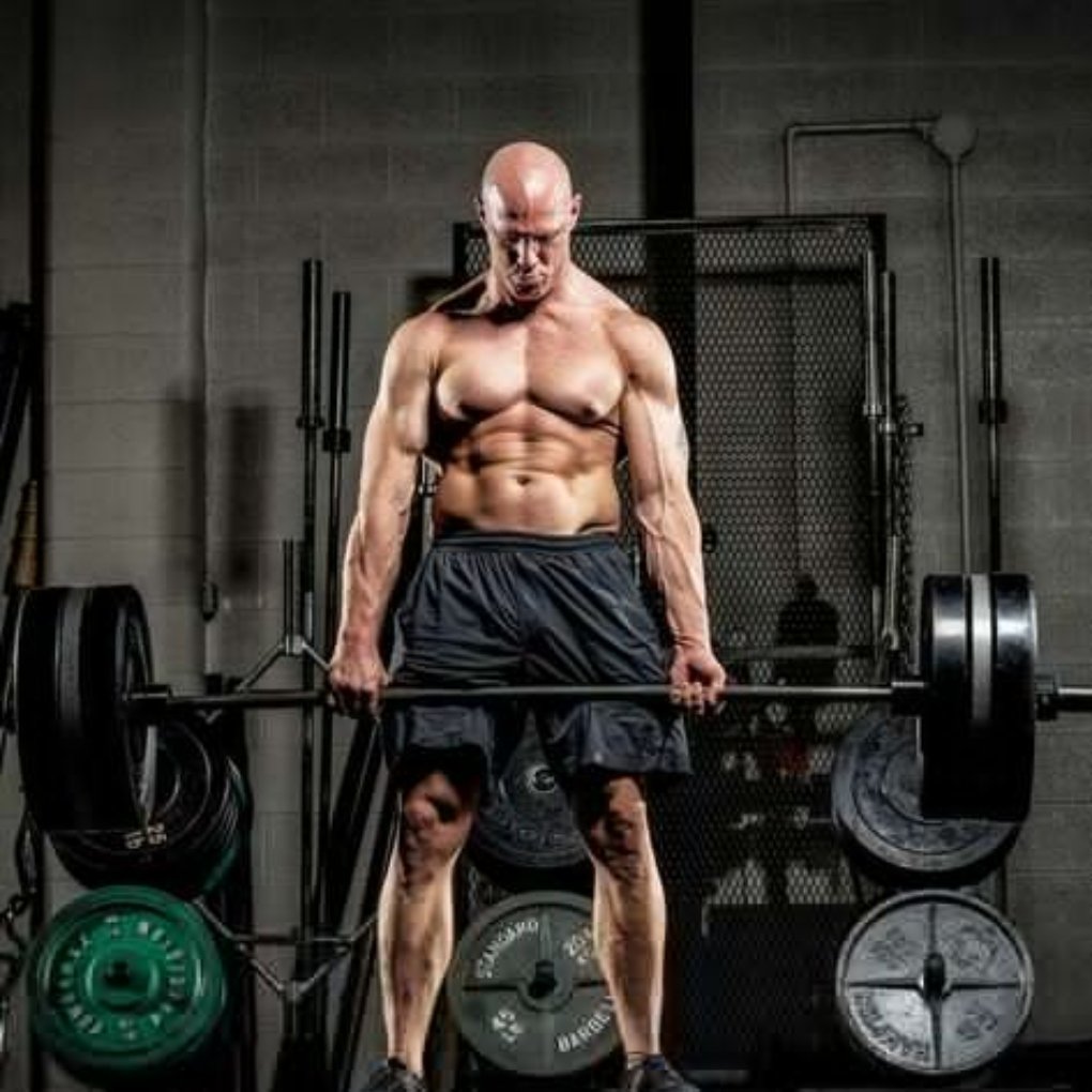 A muscular bald man lifts a heavy barbell in a gym setting, showcasing his strength and focus. gym wear guide