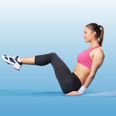 A women performs a seated exercise on a workout mat, wearing a pink top sportswear bra and black leggings.