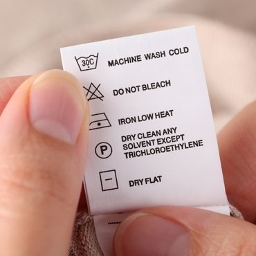 A person is holding a care label that provides washing instructions for a rayon garment.