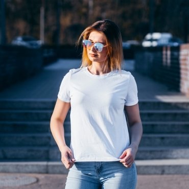 A woman wearing a white t-shirt and sunglasses stands confidently on outdoor stairs.