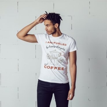 A person wearing a white t-shirt featuring a graphic design of a coffee pot with the text "I AM FUELED by happy thoughts and COFFEE."