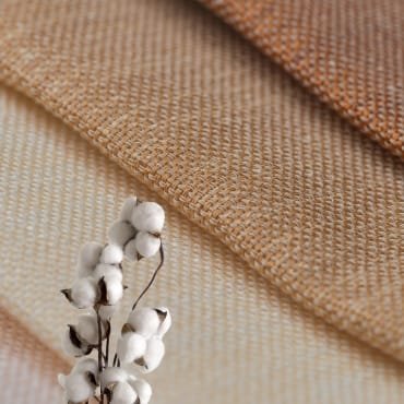 Close-up of textured cotton fabrics in warm tones, with a decorative cotton stem.