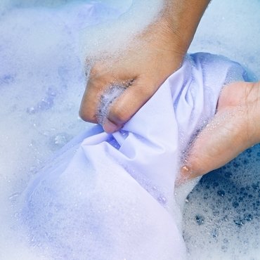A close-up of a hand washing a light purple rayon fabric in cold water.