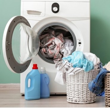 A washing machine with laundry inside, surrounded by containers of detergent and baskets of clothes.