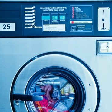 A close-up of a commercial washing machine control panel with a view of the washing drum through the window, showing colorful clothes inside.