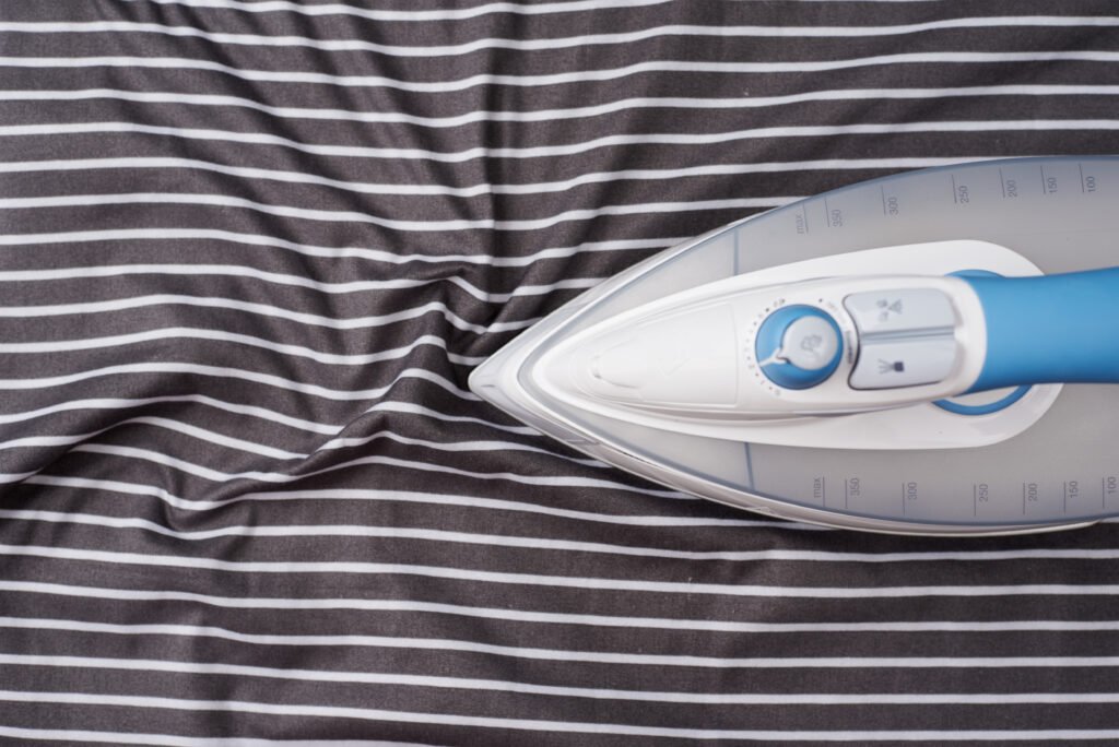 An iron placed on wrinkled gray and white striped fabric.
