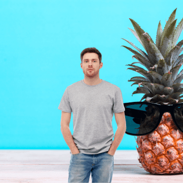 A person in a gray t-shirt stands beside a pineapple wearing sunglasses against a bright blue background.