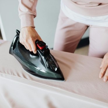Person ironing a light-colored rayon fabric with a steam iron.
