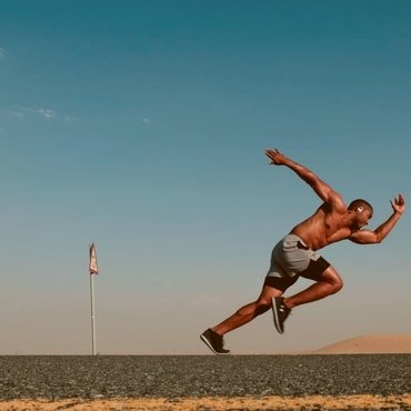 A shirtless male wear a   top sportswear short athlete sprinting on a deserted road with a clear blue sky in the background.