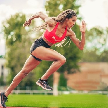An athletic woman sprinting on a track, wearing a red sports bra and black shorts.