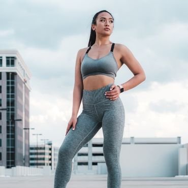 A confident woman posing in a gray sports bra and matching high-waisted leggings on a rooftop.