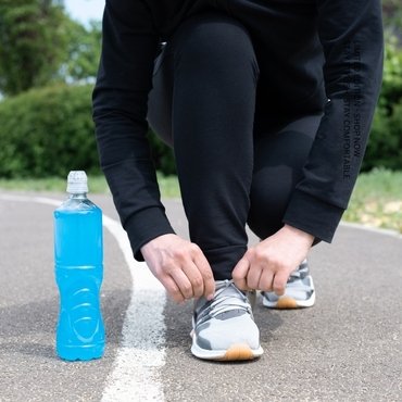 A person tying their shoelaces while kneeling on a running track next to a top sportswear tracksuit
