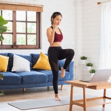 A woman in a home setting performs a workout routine. She wears a red sports bra and black leggings with a stylish cutout design.