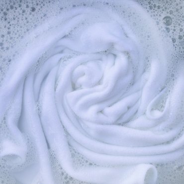 Close-up of white rayon fabric submerged in soapy water, displaying soft, swirling textures.